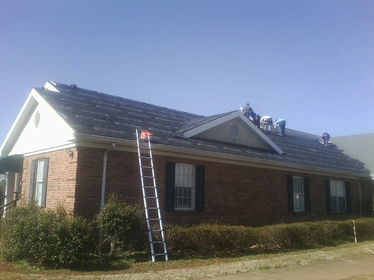 Crew tearing shingles off a brick ranch roof with a ladder set — Emergency Roof Repair work by our crew in Turlock