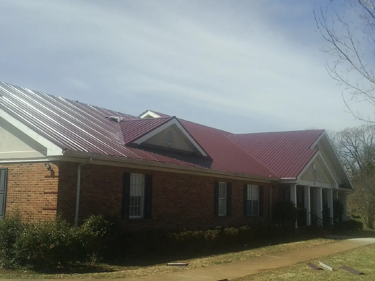 Red metal roof with gabled entries on a long brick building, from a Hail Damage Roof Repair job in Turlock